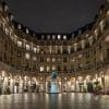Photographie d'art nocturne de la place Édouard VII à Paris avec ses arcades illuminées et sa statue centrale.