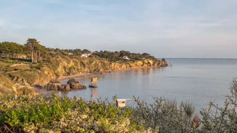 Falaises rocheuses baignées de lumière dorée, bordées de plages et de pêcheries sur pilotis sur la côte de Jade, en Loire-Atlantique.