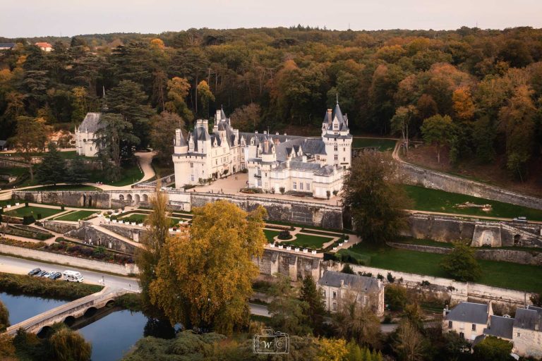 Vue aérienne plongeante sur le château blanc d'Ussé, ses terrasses avec parterres à la française, sa chapelle et la forêt aux teintes automnales.