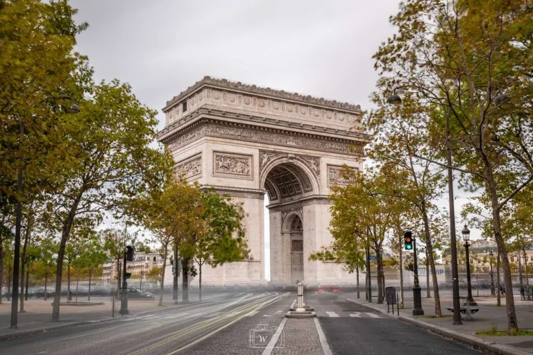 Vue centrale de l'Arc de Triomphe en automne avec traînées lumineuses de circulation en pose longue sur les pavés à Paris.