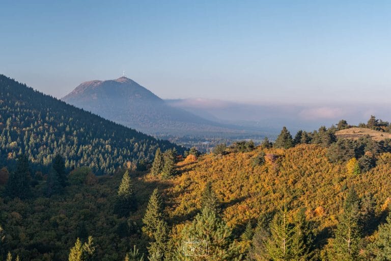 Panorama du volcan du Puy de Dôme en automne avec les couleurs orangées de la végétation et la Chaîne des Puys.