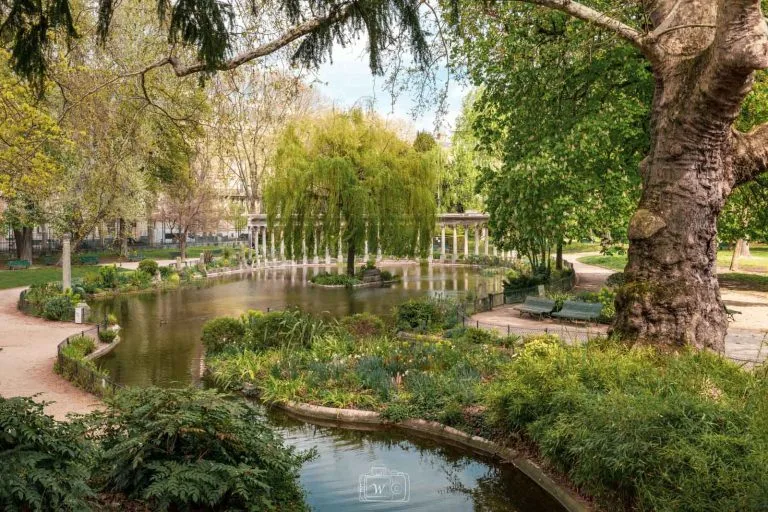 Vue de la colonnade antique et du bassin du Parc Monceau entourés de végétation verdoyante et d'un saule pleureur à Paris.