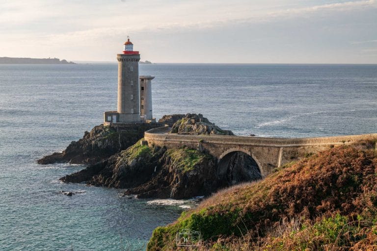 Phare du Petit Minou et son pont en pierre en courbe dominant l'océan Atlantique et la rade de Brest sous la lumière rasante du matin dans le Finistère.