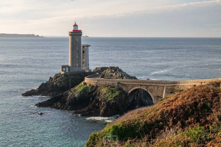 Phare du Petit Minou et son pont en pierre en courbe dominant l'océan Atlantique et la rade de Brest sous la lumière rasante du matin dans le Finistère.